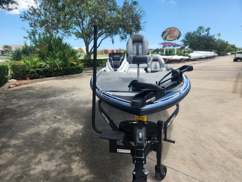 Slide: The Image of 2024 Nitro Z20 boat on trailer, parked outdoors near trees and Bass Pro Shop sign. - 2