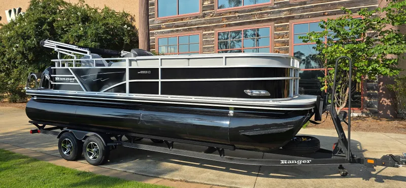 Slide: The Image of 2024 Ranger Reata 223C pontoon boat on trailer, parked outdoors. - 0