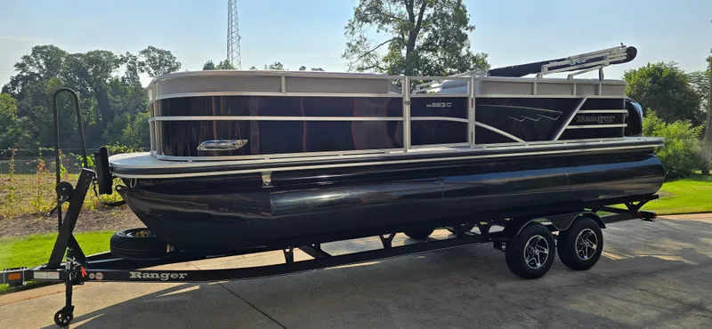 Slide: The Image of 2024 Ranger Reata 223C pontoon boat on trailer, parked outdoors. - 2