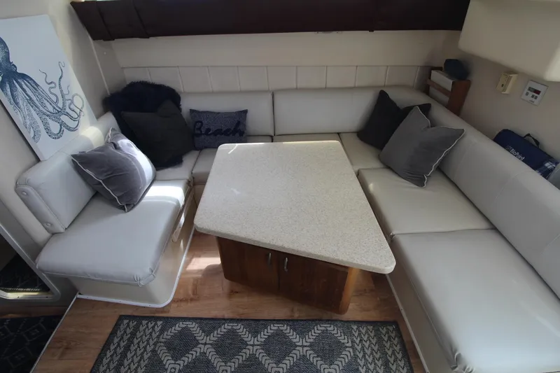 Slide: The Image of 1999 Mainship 31 Sedan Bridge interior with white seating and a central table. - 19