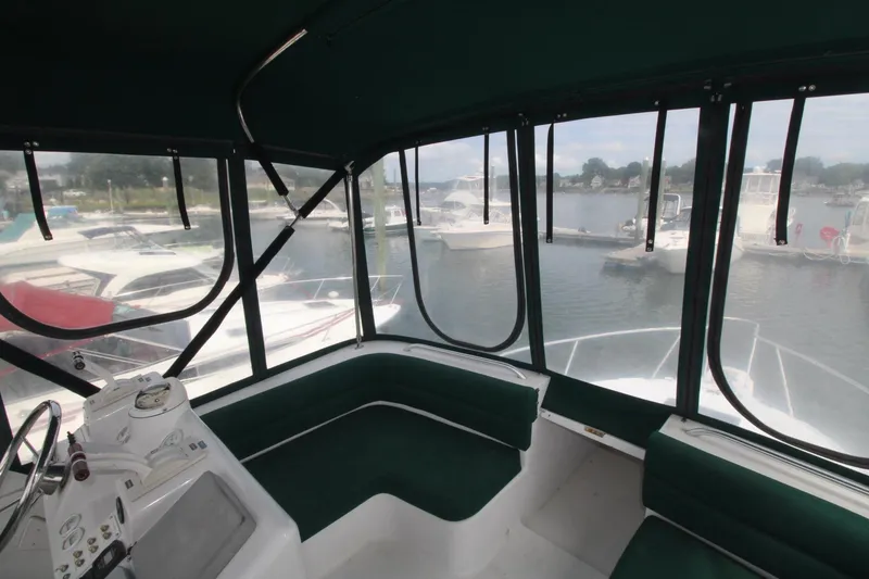 Slide: The Image of 1999 Mainship 31 Sedan Bridge interior with marina view, featuring green seating and helm controls. - 9
