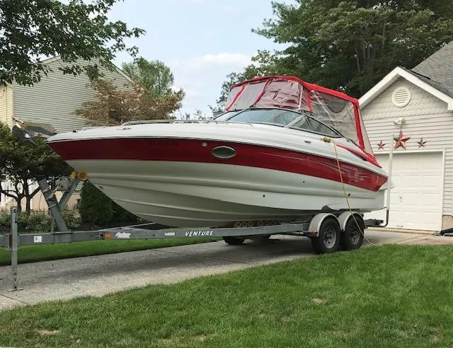 The Image of 2006 Crownline 255 CCR boat on trailer, red and white design, parked in driveway. - 0
