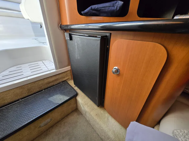 Slide: The Image of Interior of a 2006 Crownline 255 CCR boat, featuring a compact fridge and wooden cabinetry. - 18