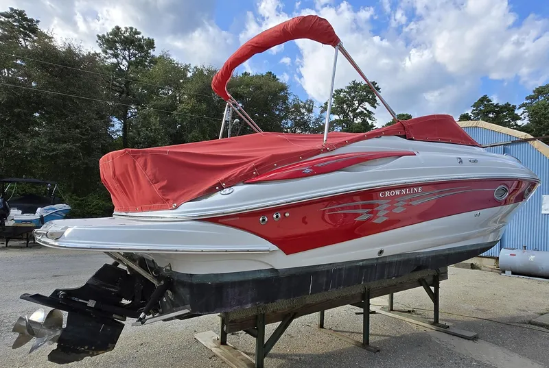 Slide: The Image of 2006 Crownline 255 CCR boat with red cover, parked outdoors on a stand. - 2