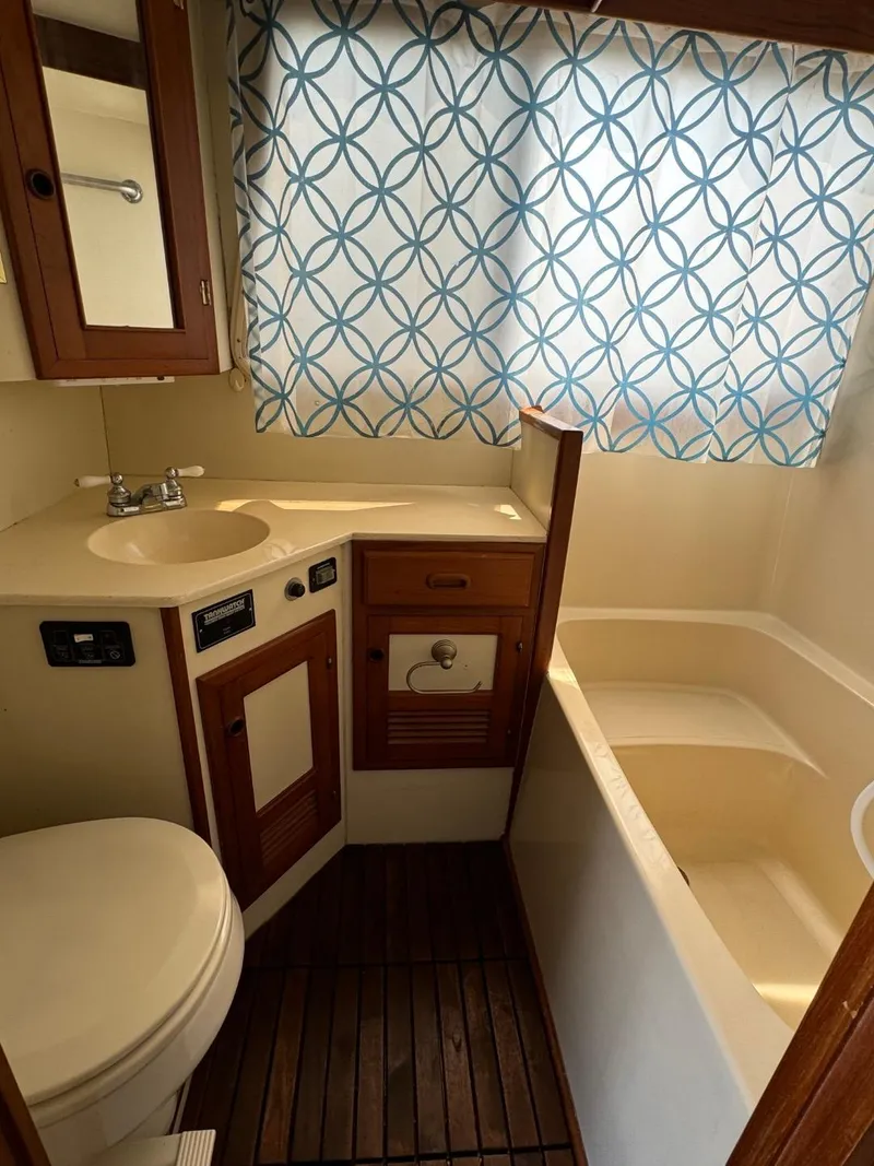 Slide: The Image of 1987 Kadey-Krogen Silhouette bathroom with wooden accents, sink, toilet, and patterned curtain. - 21