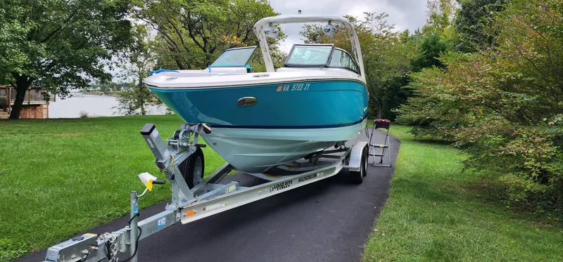 Slide: The Image of 2023 Regal LS6 boat on trailer, parked on a driveway surrounded by greenery. - 2