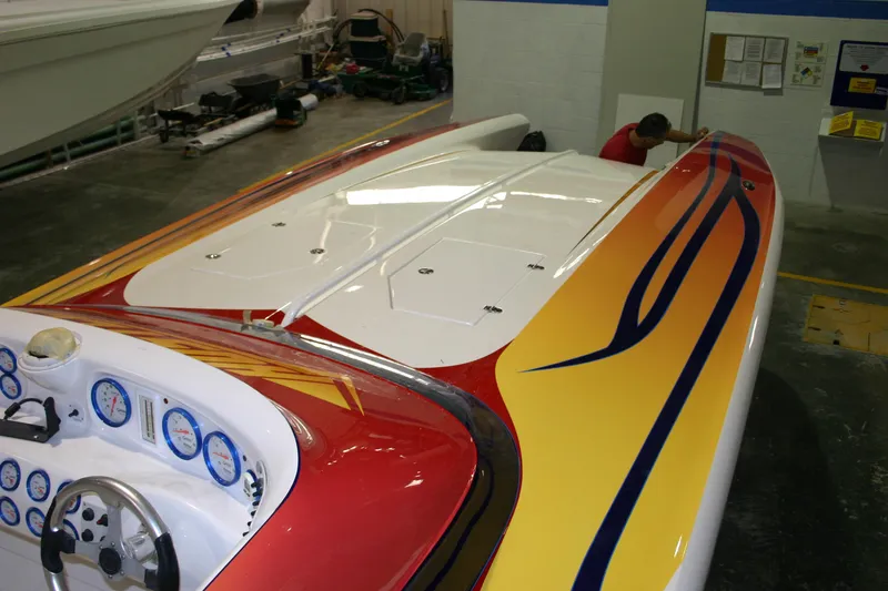 Slide: The Image of 2003 Hustler 377 Talon speedboat with vibrant red and yellow design in a workshop. - 5
