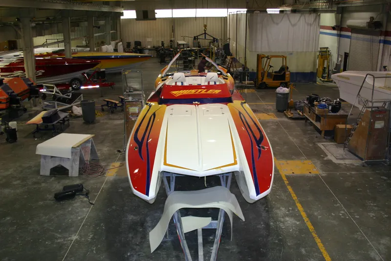 Slide: The Image of 2003 Hustler 377 Talon speedboat in a workshop, vibrant red and yellow design. - 6