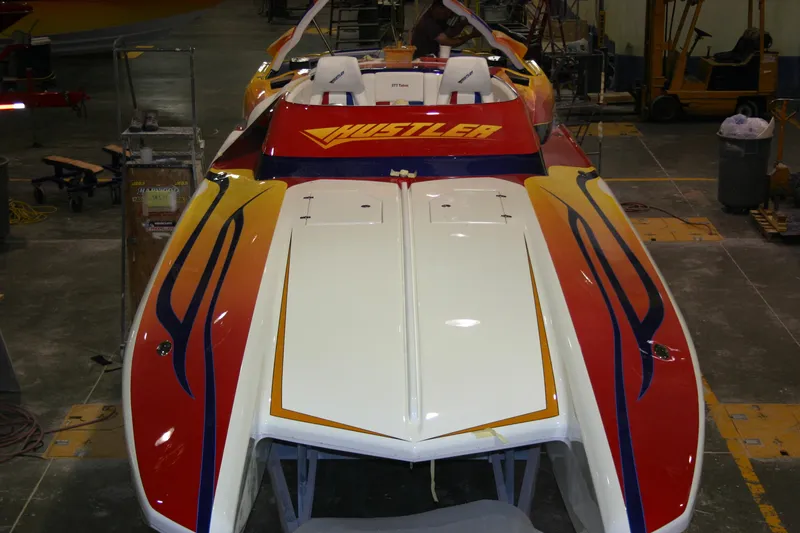 Slide: The Image of 2003 Hustler 377 Talon speedboat with vibrant red and yellow design in a workshop. - 7