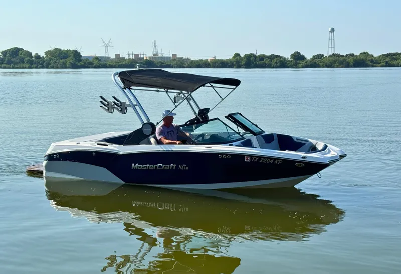 The Image of 2022 MasterCraft NXT20 boat on calm lake with canopy and wakeboard rack. - 0