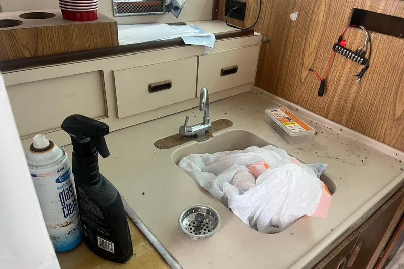 Slide: The Image of 1973 Bertram 28 Flybridge Cruiser kitchen sink area with cleaning supplies and clutter. - 36