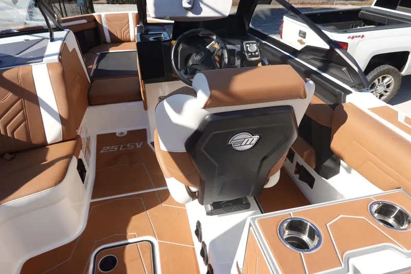 Slide: The Image of 2025 Malibu Wakesetter 25 LSV interior with brown and white seating, steering wheel, and cup holders. - 16