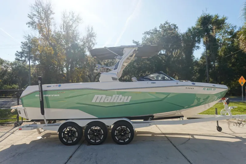 Slide: The Image of 2025 Malibu Wakesetter 25 LSV boat on trailer, green and white design, parked outdoors. - 5