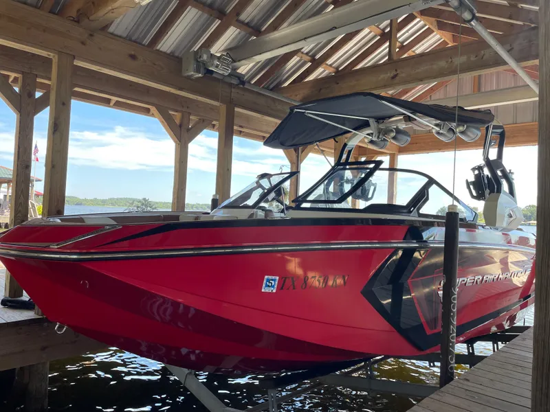 Slide: The Image of 2019 Nautique Super Air Nautique G23 Coastal Edition in red, docked under a wooden shelter. - 1
