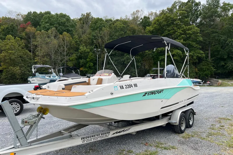 The Image of 2024 Starcraft SVX 211 OB boat on trailer, parked outdoors with trees in background. - 10