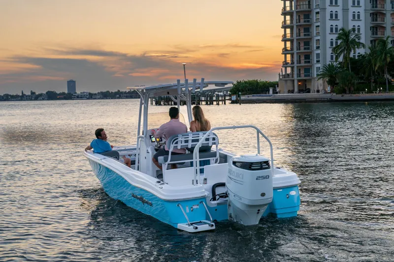 Slide: The Image of 2025 NauticStar 231 Hybrid boat cruising at sunset near waterfront buildings. - 21