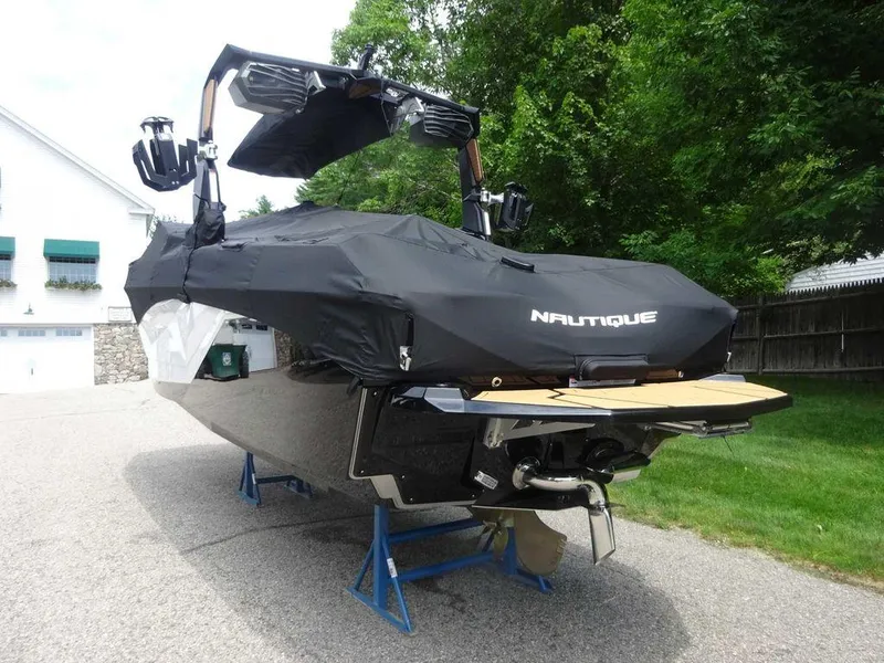 Slide: The Image of 2025 Nautique G23 boat covered, parked on stands, in a driveway with greenery. - 5