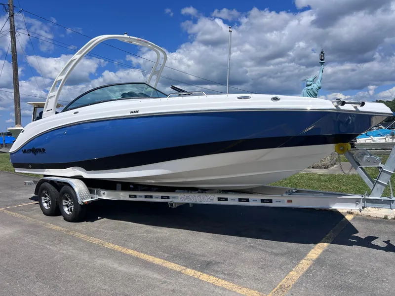 The Image of 2025 NauticStar 243 DC Deck boat on trailer, blue and white, parked outdoors. - 0