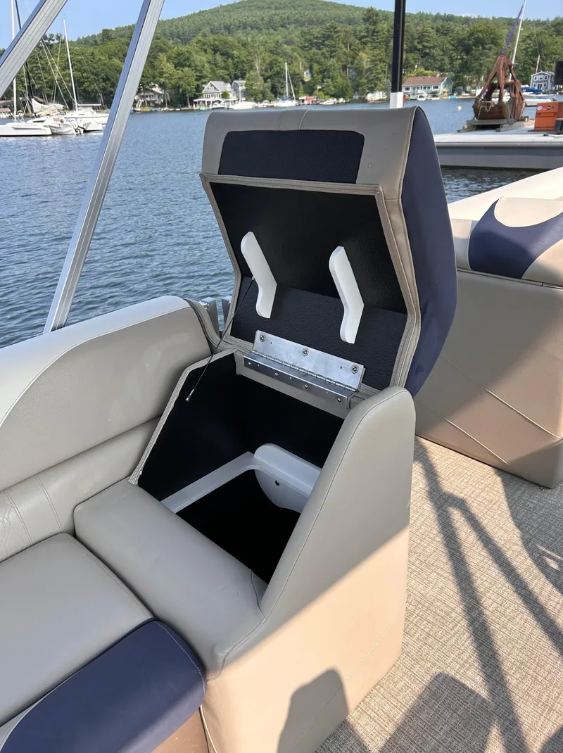 Slide: The Image of 2024 Avalon LSZ Cruise 25' boat seat with open storage compartment by a lake. - 16