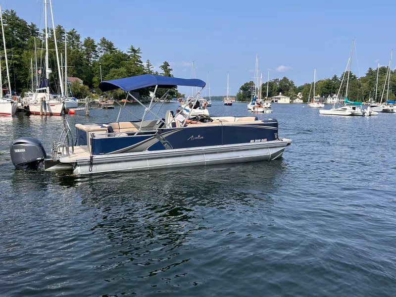 Slide: The Image of 2024 Avalon LSZ Cruise 25' pontoon boat on a scenic lake with sailboats. - 2