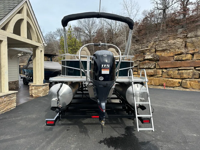 Slide: The Image of 2024 Starcraft LX 22 F pontoon boat with 115 HP engine, parked on a trailer. - 1