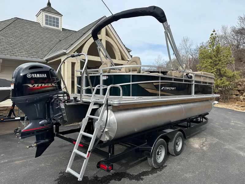 Slide: The Image of 2024 Starcraft LX 22 F pontoon boat with Yamaha engine on trailer, parked near house. - 2