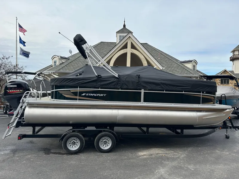 Slide: The Image of 2024 Starcraft LX 22 F pontoon boat on trailer, covered, parked near a building. - 6