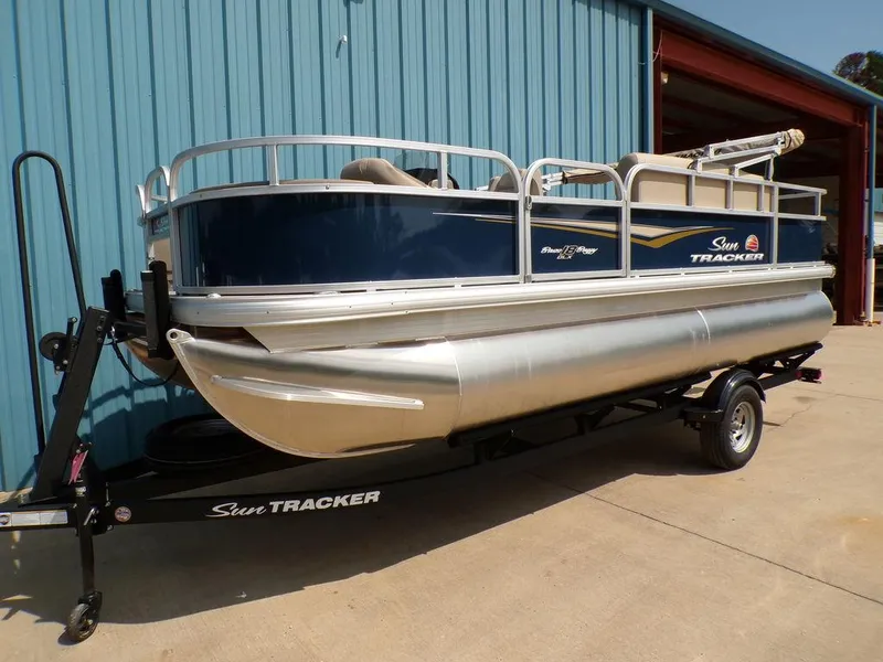 The Image of 2024 Sun Tracker BASS BUGGY® 18 DLX pontoon boat on trailer, parked by blue building. - 1