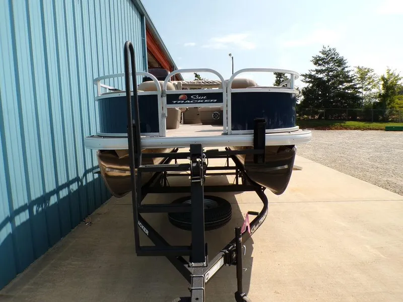Slide: The Image of 2024 Sun Tracker BASS BUGGY® 18 DLX pontoon boat on trailer, parked beside blue building. - 3