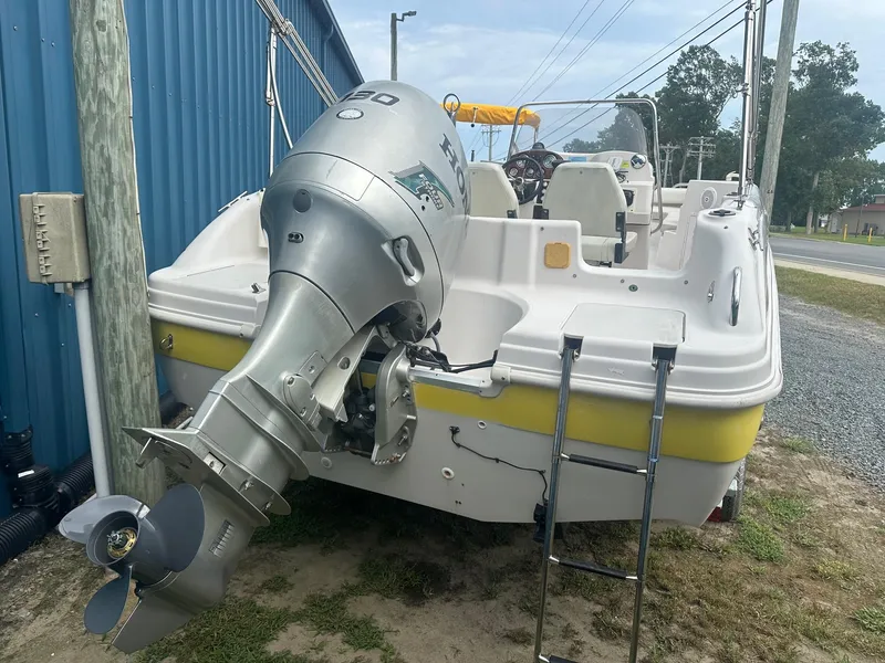 Slide: The Image of 2003 Godfrey Hurricane FD211 boat with outboard motor and ladder, parked near a blue building. - 2