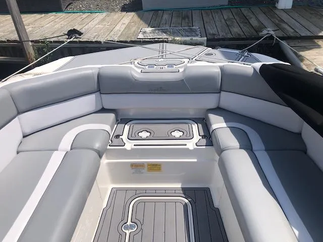 Slide: The Image of 2022 NauticStar 243 DC boat interior with gray and white seating, docked by wooden pier. - 9