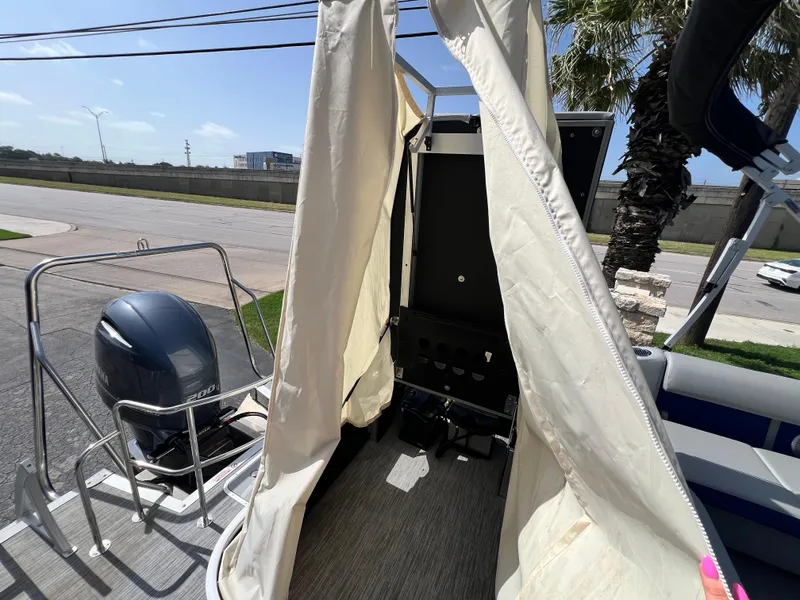 Slide: The Image of 2022 Bennington 23LSB boat interior with engine and canopy, parked outdoors. - 15
