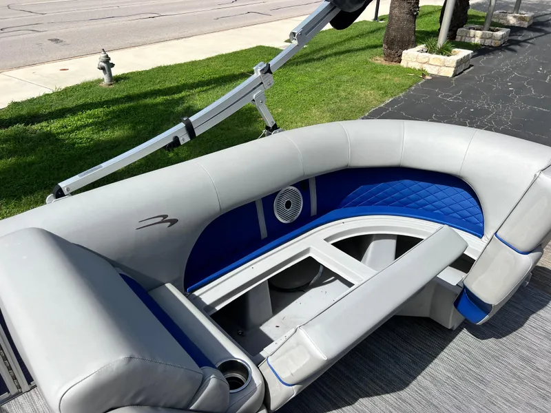 Slide: The Image of 2022 Bennington 23LSB boat interior with gray and blue seating, cup holders, and speaker. - 21