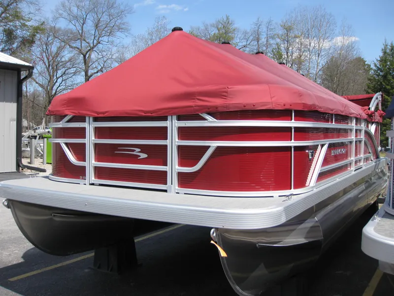 Slide: The Image of 2024 Bennington 20SVSRSR pontoon boat with red cover, parked outdoors. - 2