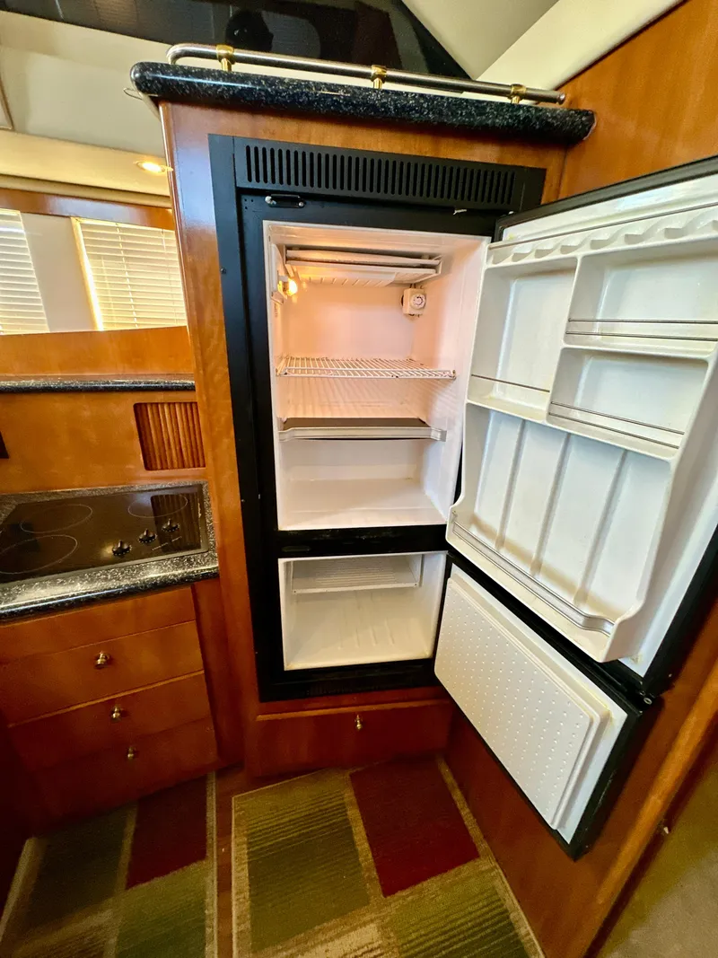 Slide: The Image of 2000 Carver 396 Motor Yacht kitchen with open refrigerator and wooden cabinetry. - 21