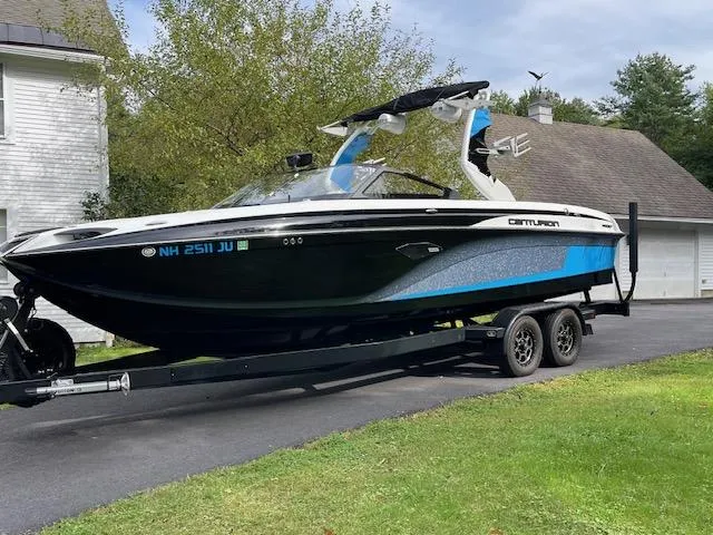 Slide: The Image of 2020 Centurion Ri237 boat on trailer parked in driveway, featuring sleek black and blue design. - 2