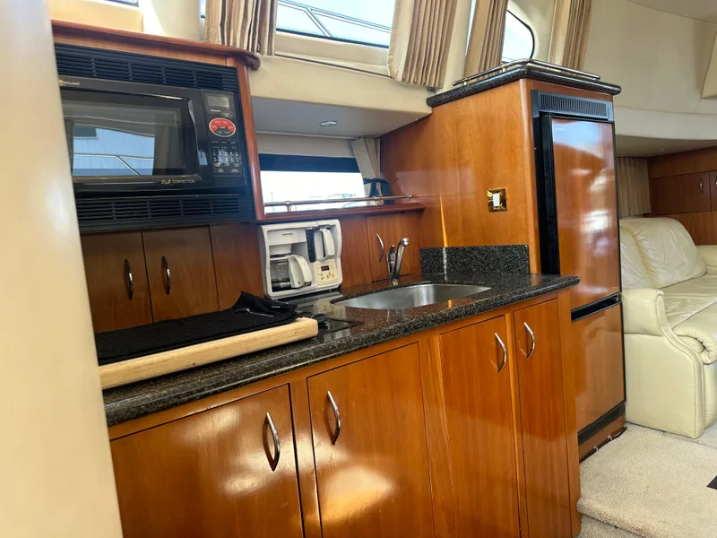 Slide: The Image of 2004 Carver 420 Mariner yacht interior with kitchenette, featuring wood cabinets and modern appliances. - 9