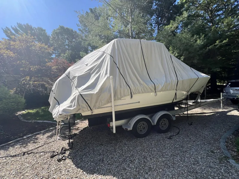Slide: The Image of 2018 Pioneer 222 Islander boat covered on a trailer in a sunny, wooded area. - 10