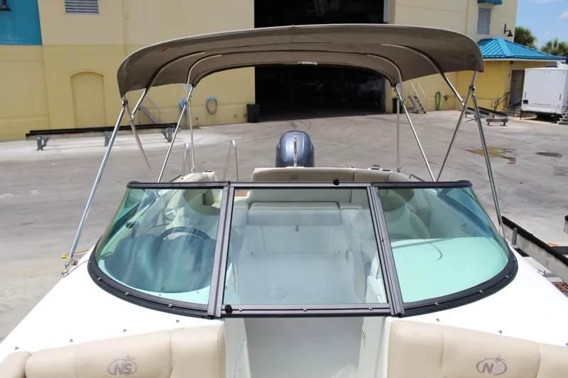 Slide: The Image of 2017 NauticStar 243DC Sport Deck boat with bimini top in a marina setting. - 22