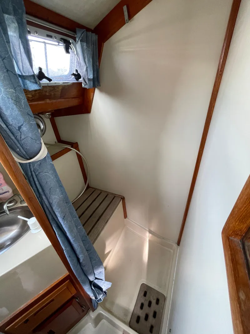 Slide: The Image of 1990 Ericson 38-200 yacht bathroom with shower, sink, and blue curtains. - 23