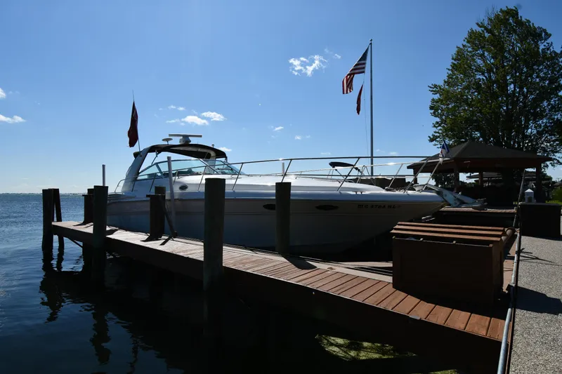 The Image of 1997 Sea Ray 400 Sundancer docked by a wooden pier under a clear blue sky. - 0