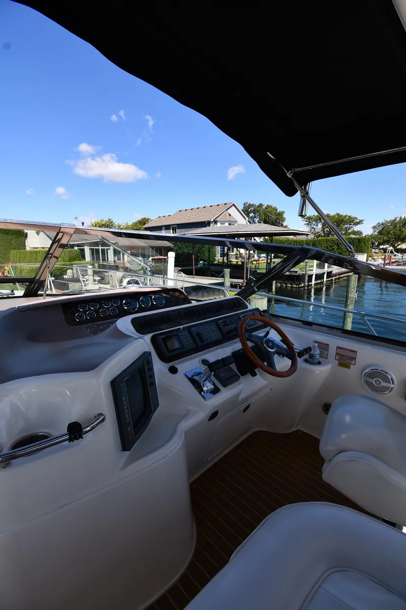 Slide: The Image of 1997 Sea Ray 400 Sundancer helm with modern controls, docked by a scenic waterfront. - 11