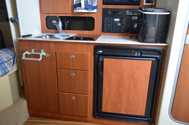 Slide: The Image of 2007 Bayliner 325 Sunbridge galley with wood cabinets, sink, stove, and mini fridge. - 31