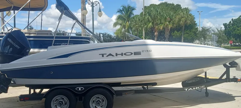The Image of 2024 Tahoe 2150 boat on trailer, parked outdoors with palm trees in background. - 0