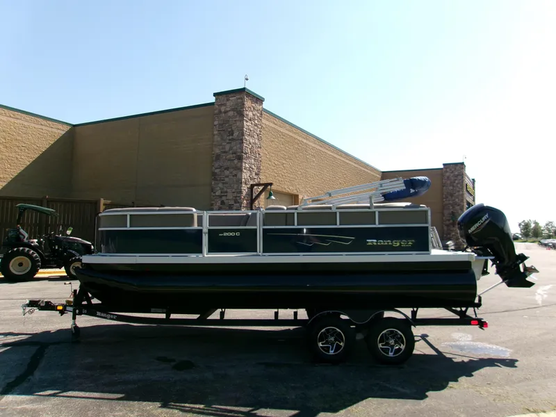 Slide: The Image of 2024 Ranger Reata 200C pontoon boat on trailer, parked outdoors. - 1