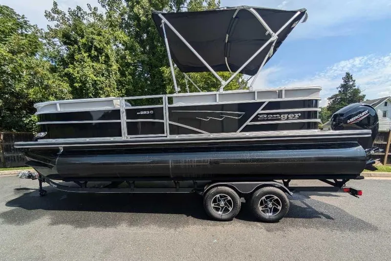 Slide: The Image of 2024 Ranger Reata 223C pontoon boat with canopy on trailer, parked outdoors. - 1