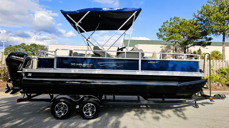 Slide: The Image of 2024 Ranger Reata 200F pontoon boat with canopy on trailer, parked outdoors. - 0