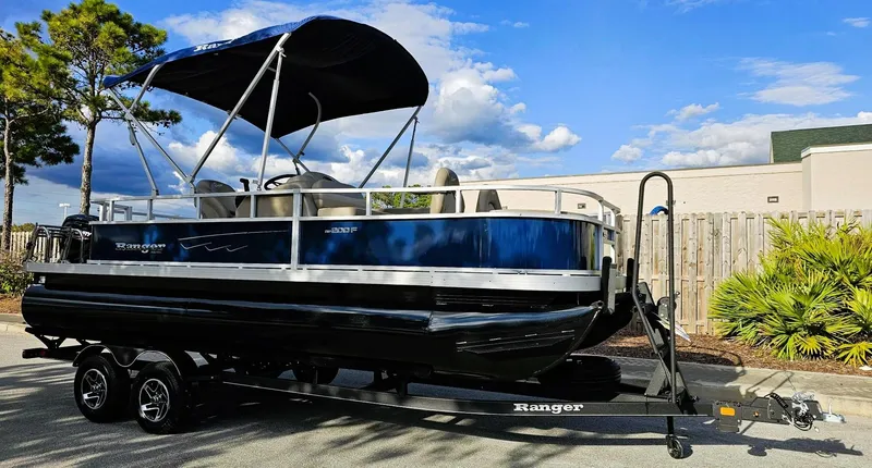 Slide: The Image of 2024 Ranger Reata 200F pontoon boat on trailer, parked outdoors. - 2