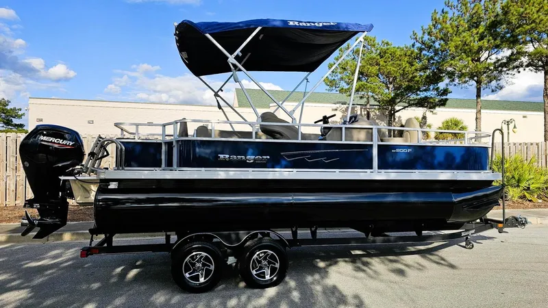 Slide: The Image of 2024 Ranger Reata 200F pontoon boat with canopy, parked on a trailer, under a clear sky. - 3