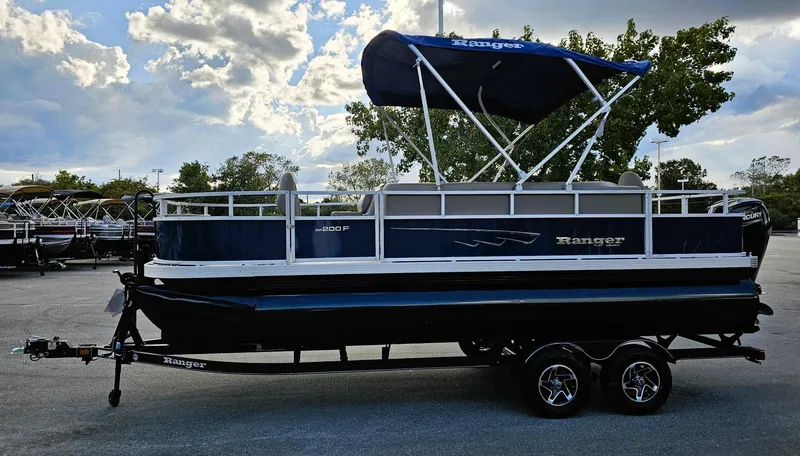 Slide: The Image of 2024 Ranger Reata 200F pontoon boat with canopy on trailer, parked outdoors. - 6